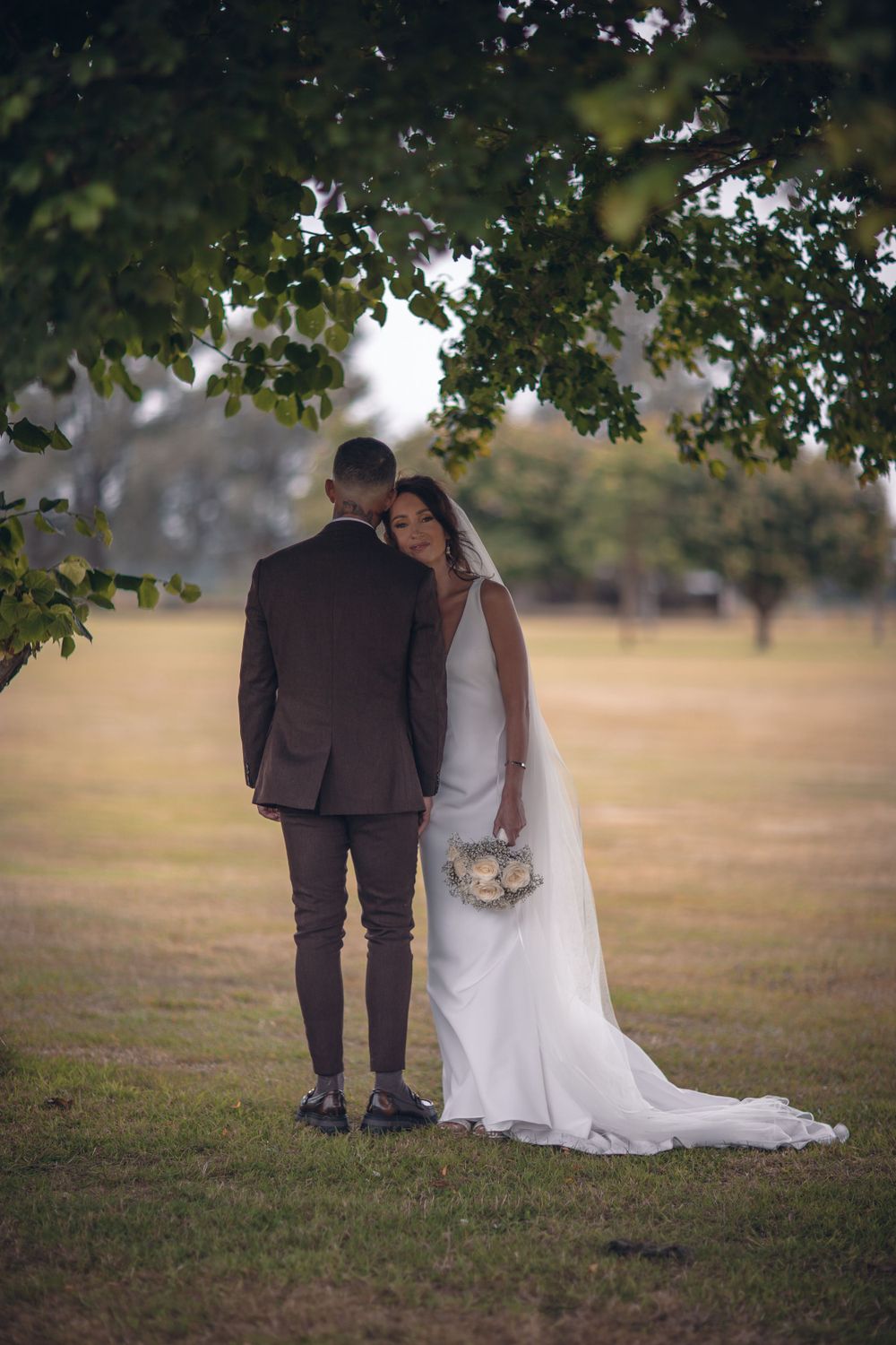 Intimate wedding portrait under tree branches in golden afternoon light.