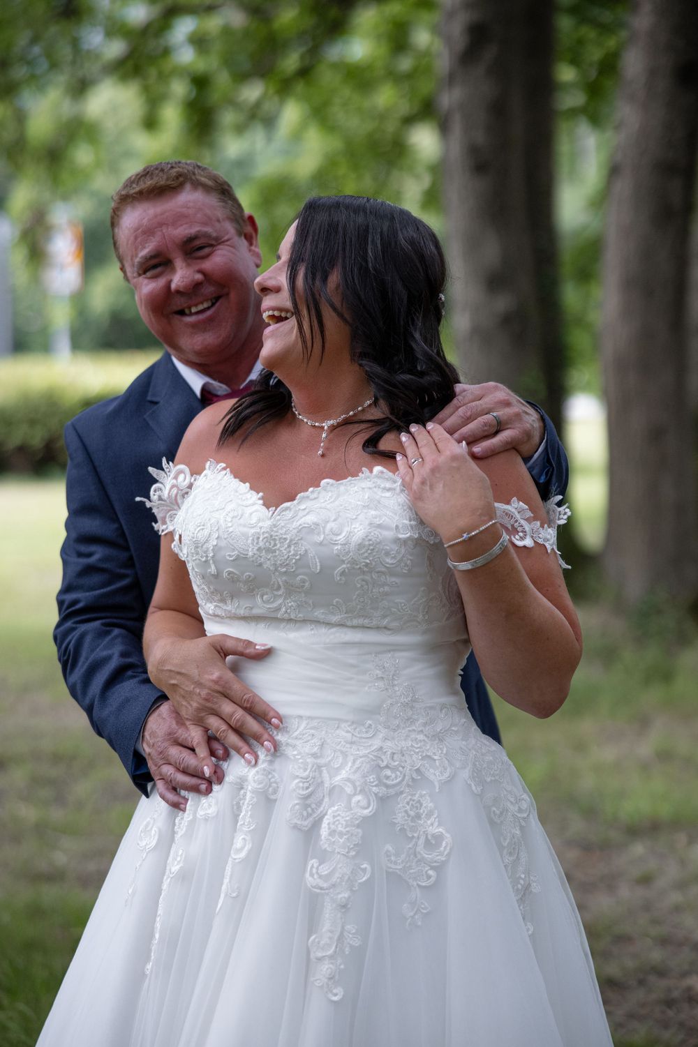 Joyful wedding couple embracing outdoors among trees.