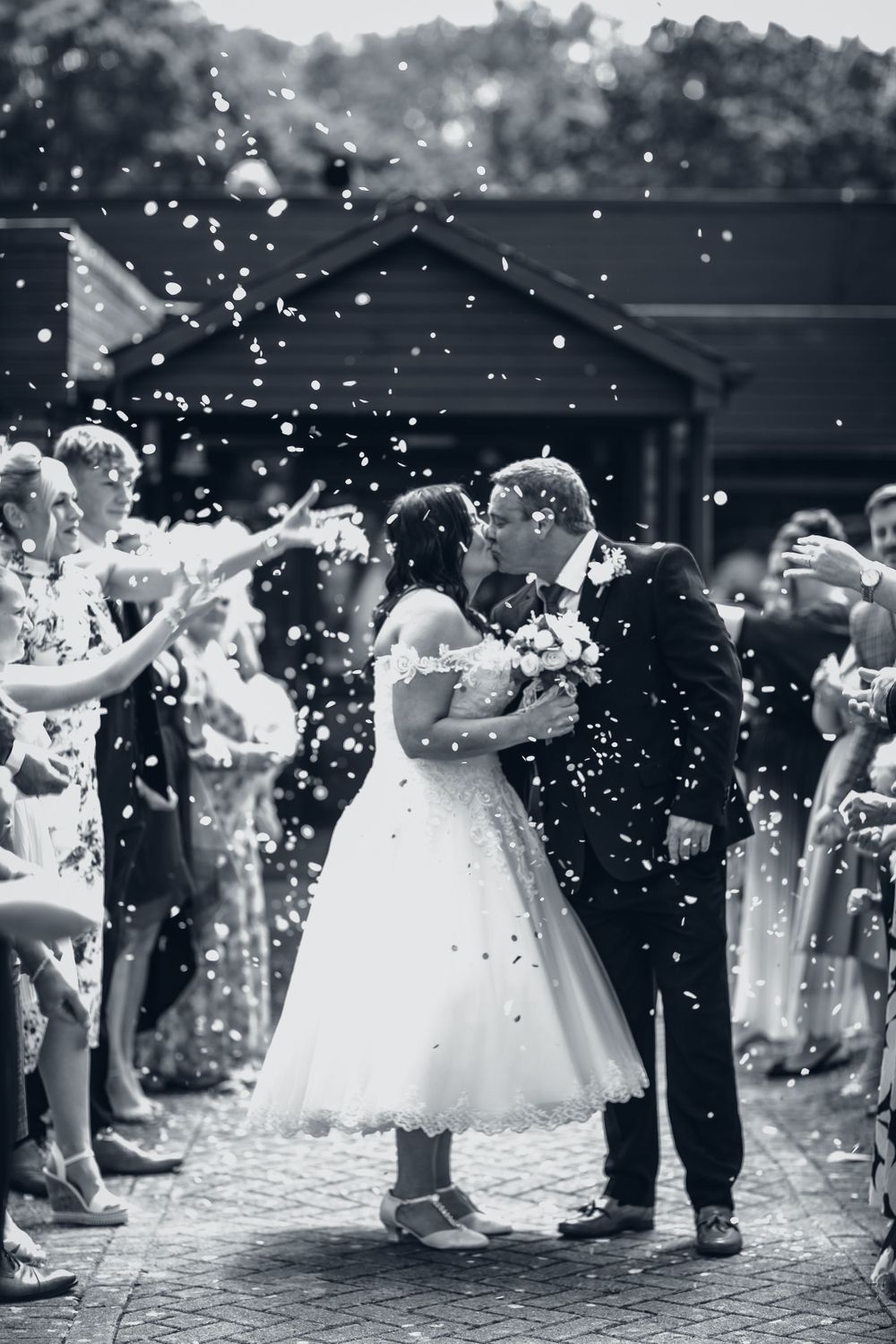 Black and white wedding photo capturing confetti moment during outdoor celebration.