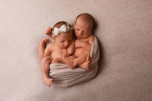Two sleeping newborns wrapped in soft gray fabric lie close together.