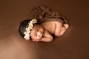 Sleeping newborn with floral crown posed on brown background.