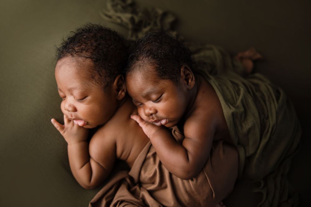 Two sleeping newborn babies lying side by side on a brown blanket against dark green backdrop. Arkansas Newborn Photographer