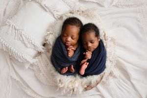 Twin newborn babies lying side by side on a blue blanket against boho backdrop. Arkansas Newborn Photographer