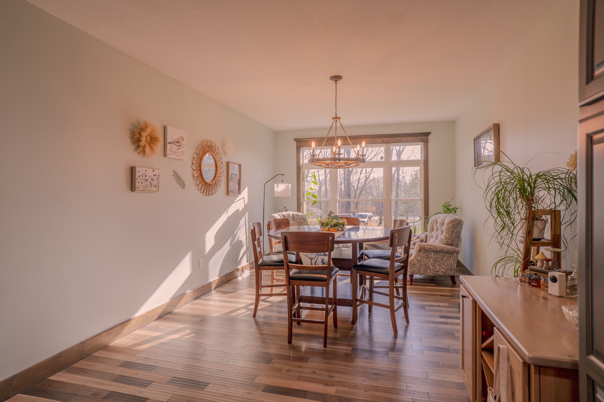 Sunlit dining room with hardwood floors, round wooden table, chairs, and a chandelier near large sliding glass doors.