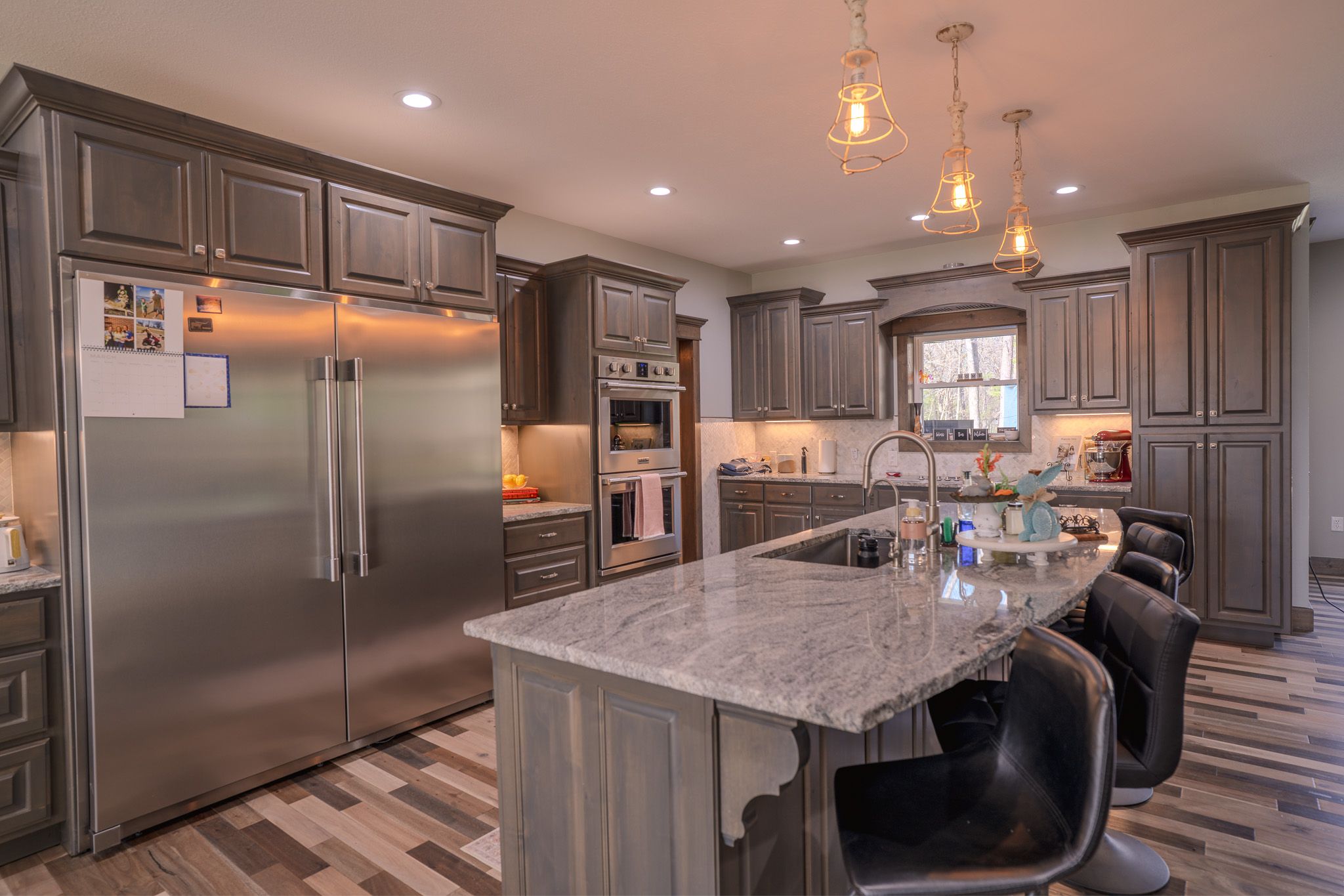 Modern kitchen with gray cabinets, stainless steel appliances, granite island, and pendant lighting over breakfast bar.