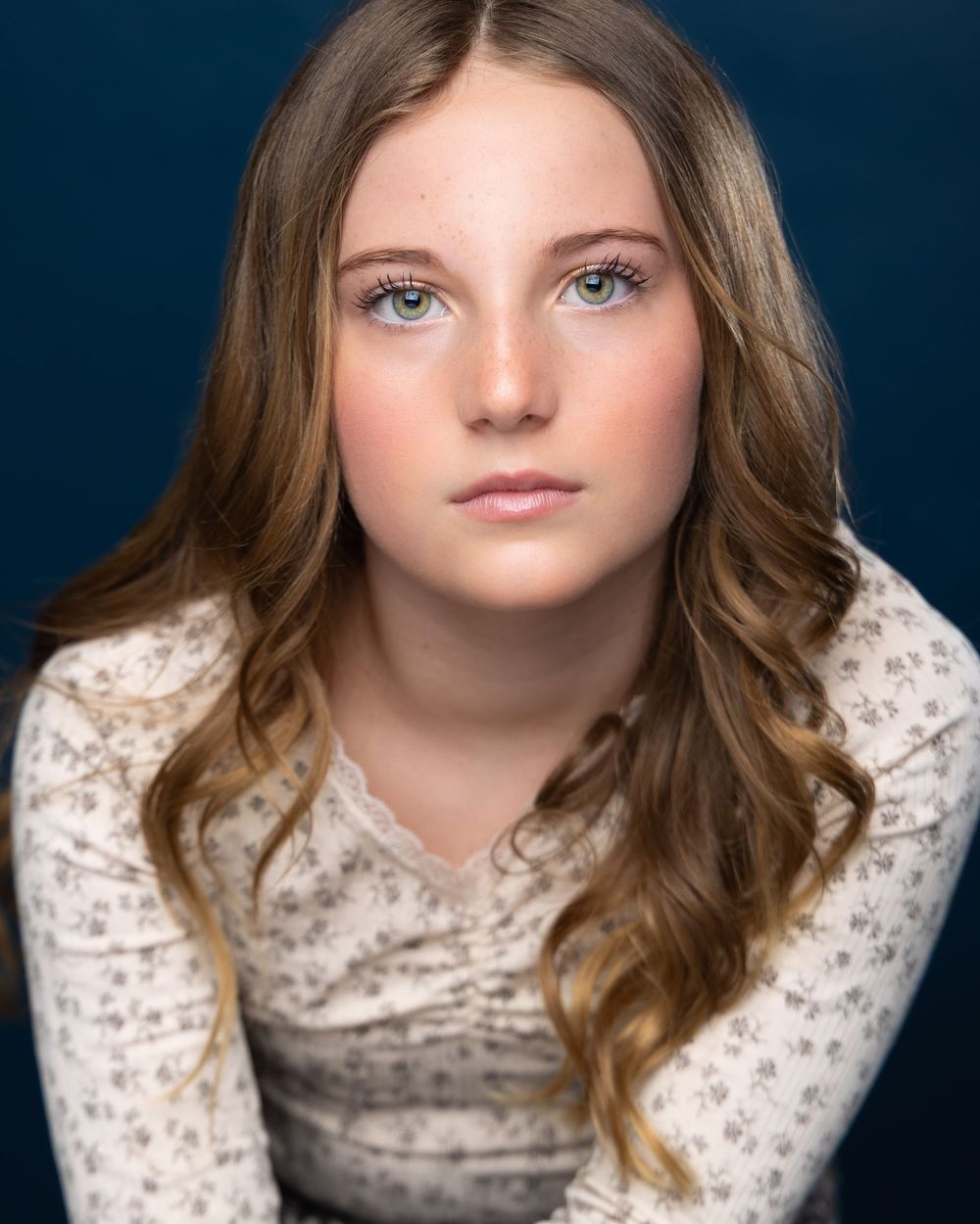 Young girl with green eyes and wavy brown hair poses for a professional headshot in a floral top.