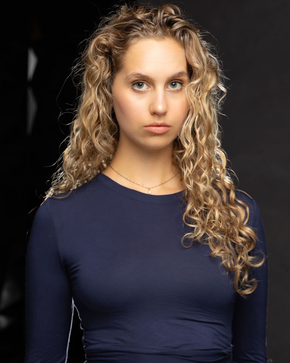 Studio portraits in navy top against dark background with dramatic lighting.