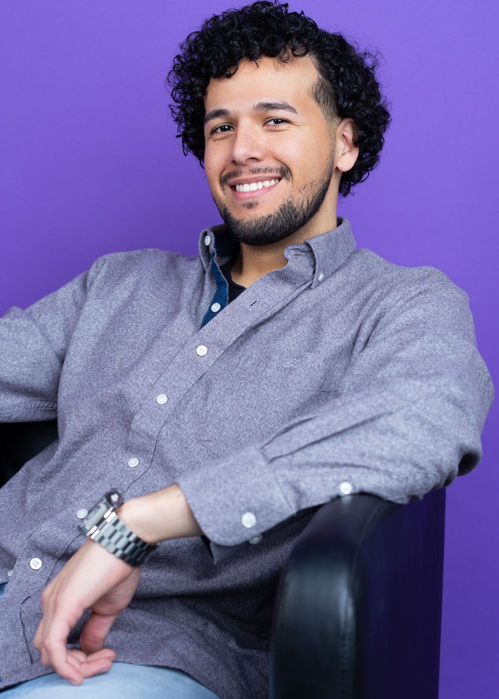 Professional headshots of person in gray shirt seated against purple background.