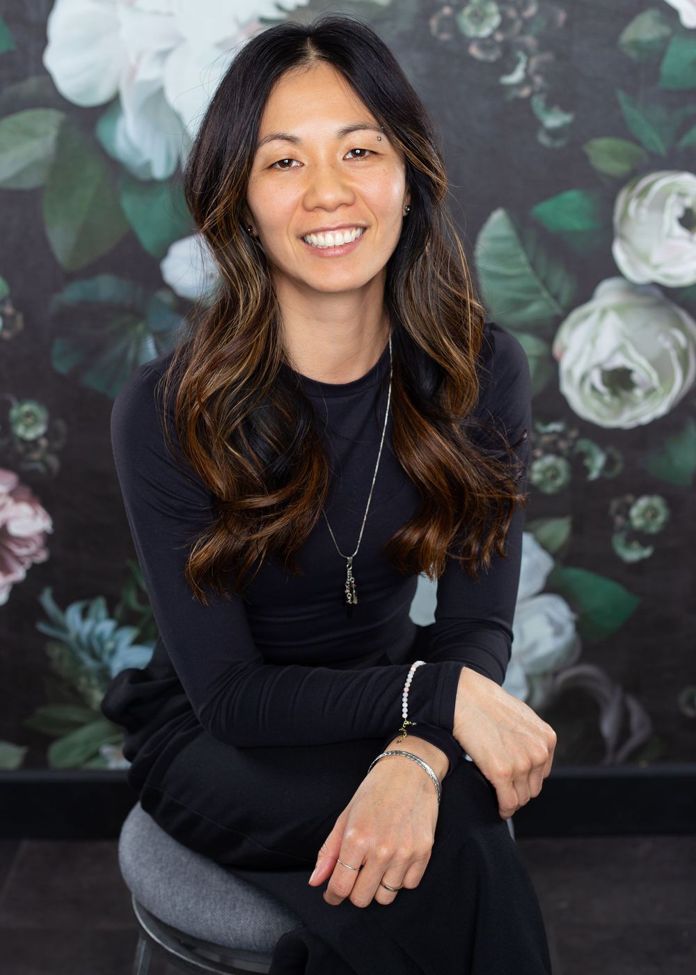 Professional headshots of person in black turtleneck against floral wallpaper background.