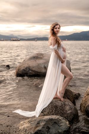 Pregnant woman in flowy dress walking barefoot on Kitsilano Beach at sunset