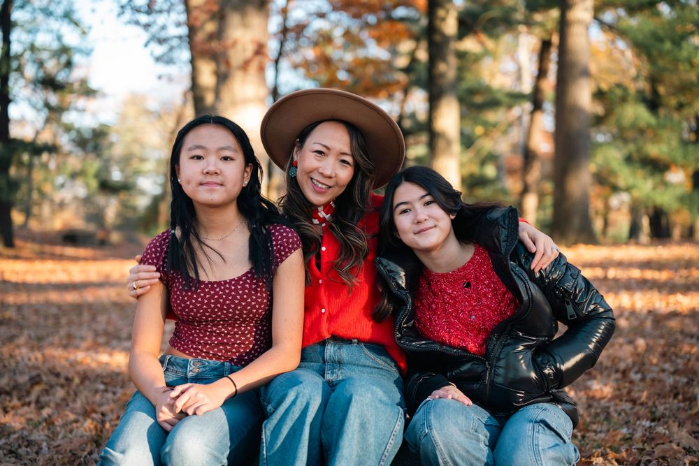 Three friends in coordinated red outfits pose together on autumn leaves in a wooded setting.