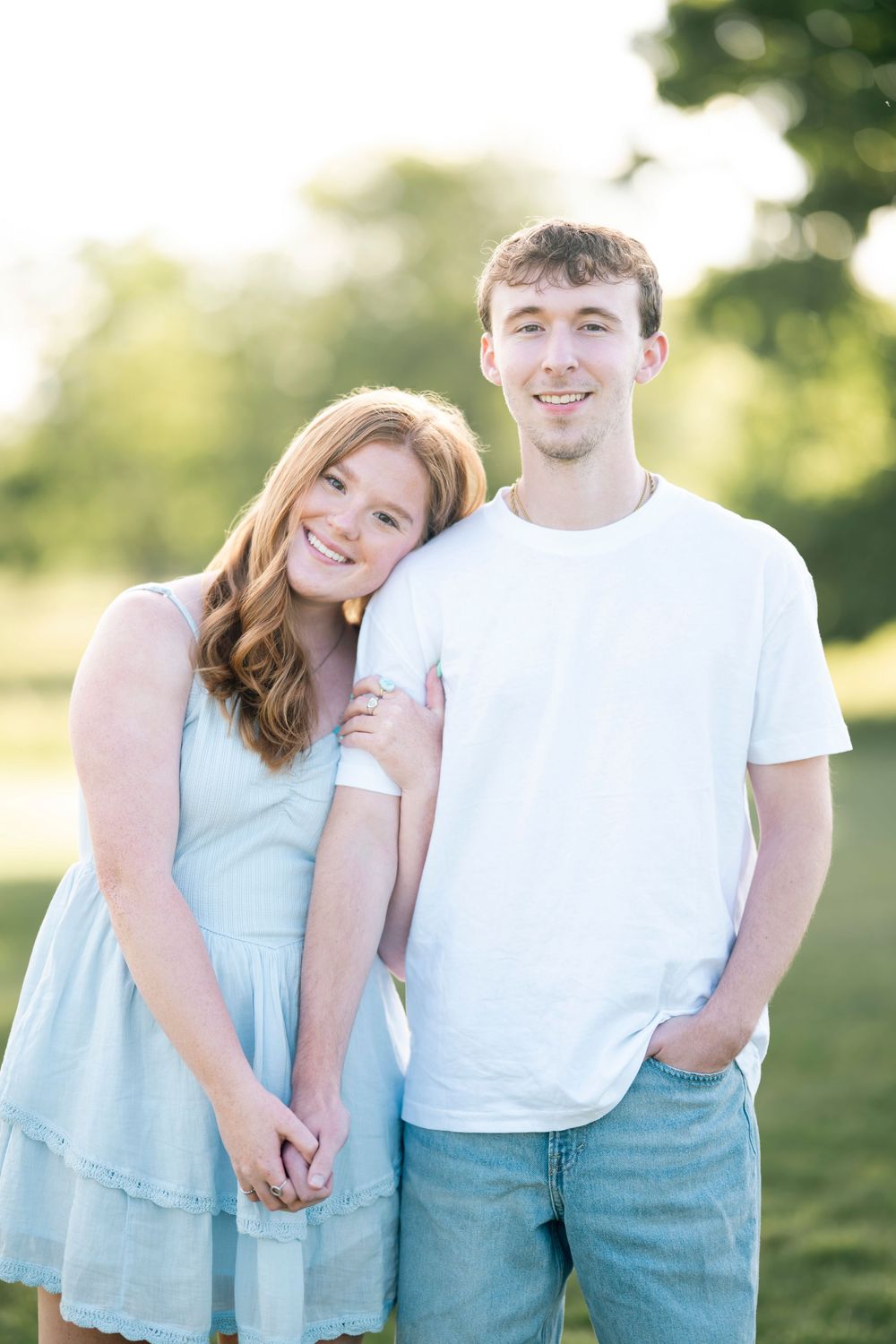 Couple in coordinating light blue and white outfits poses playfully together outdoors in natural sunlight.
