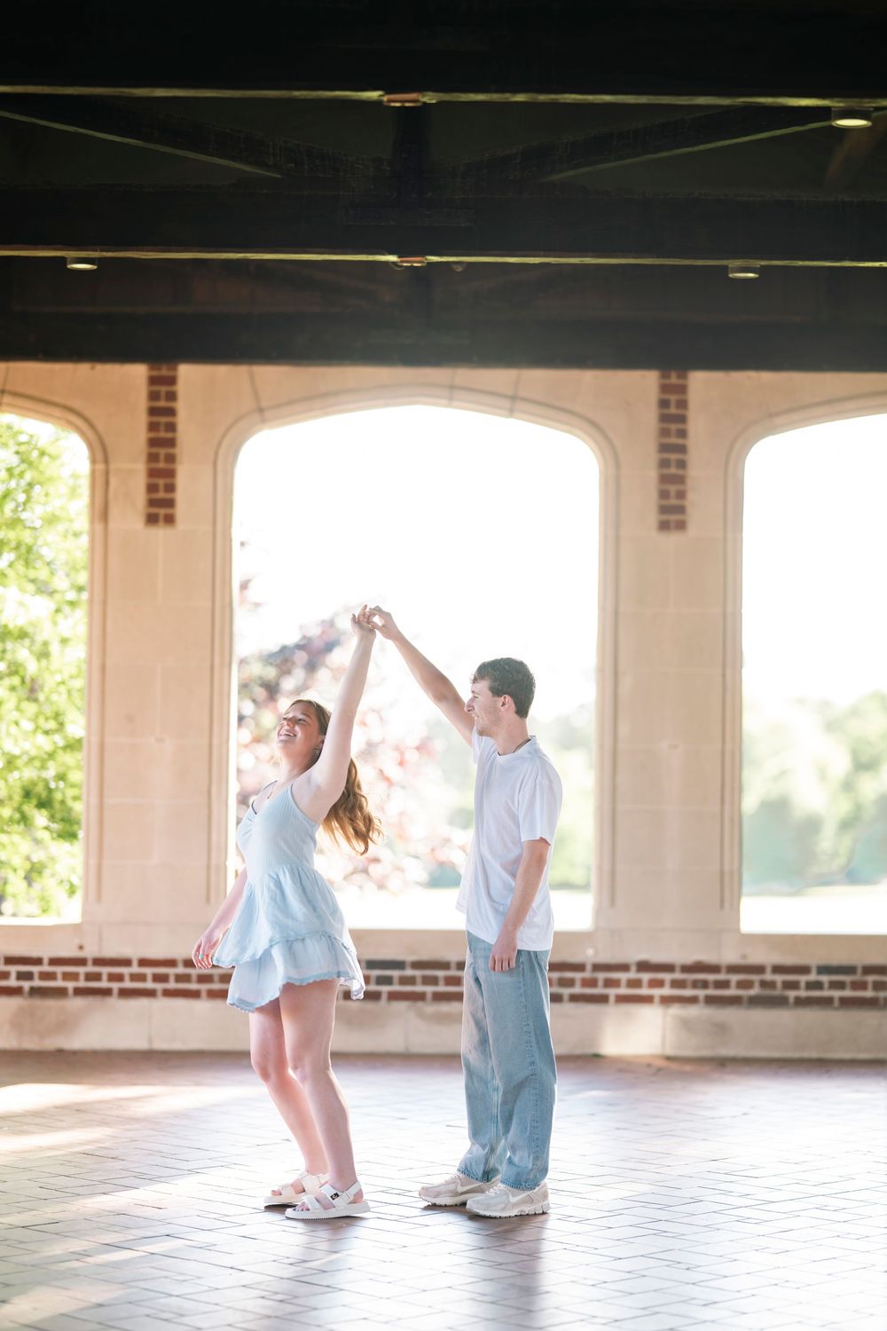 A couple shares a dance moment together in a covered outdoor space with arched windows and brick columns.
