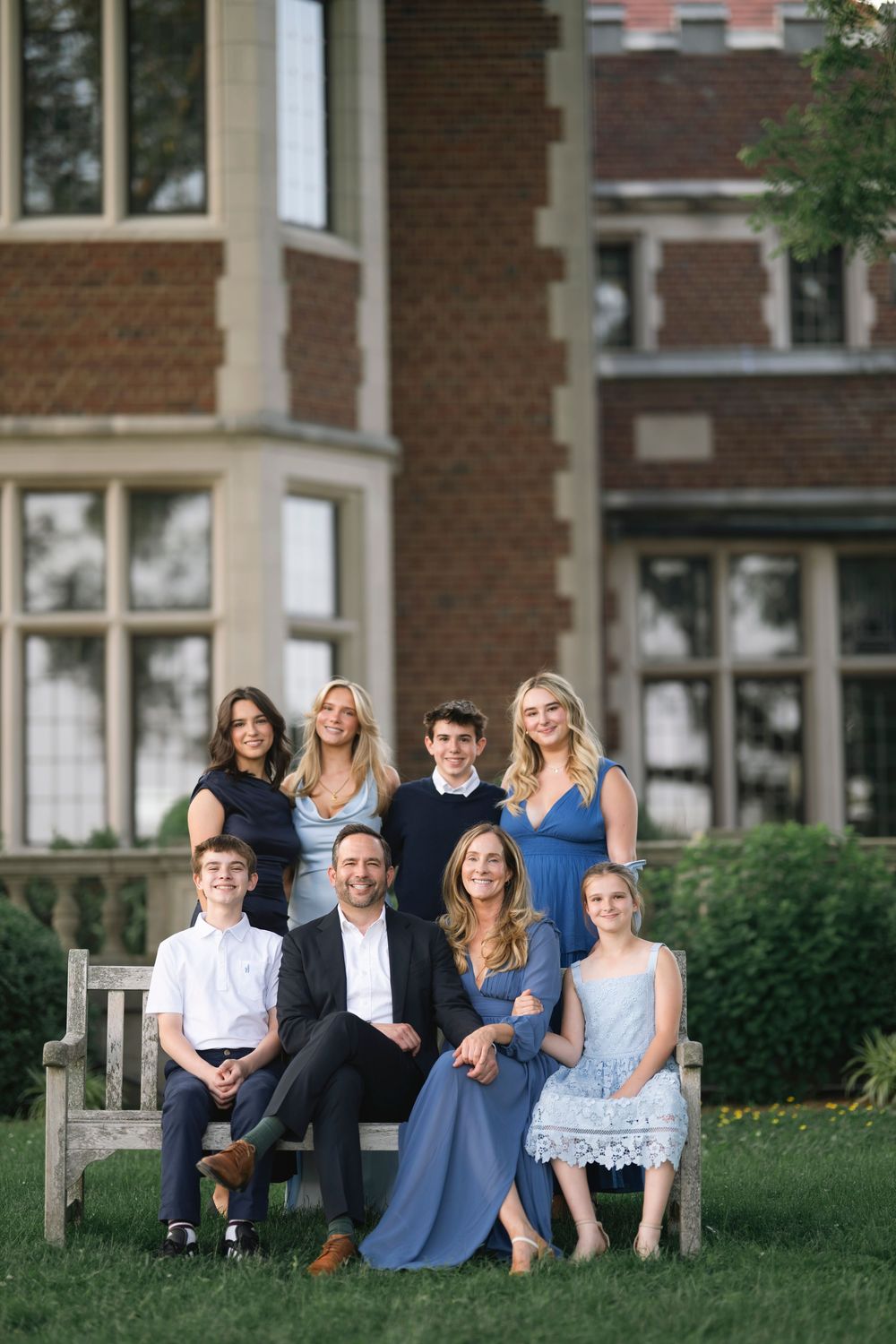 A group relaxes together on a grassy lawn outside a brick building on a sunny afternoon.