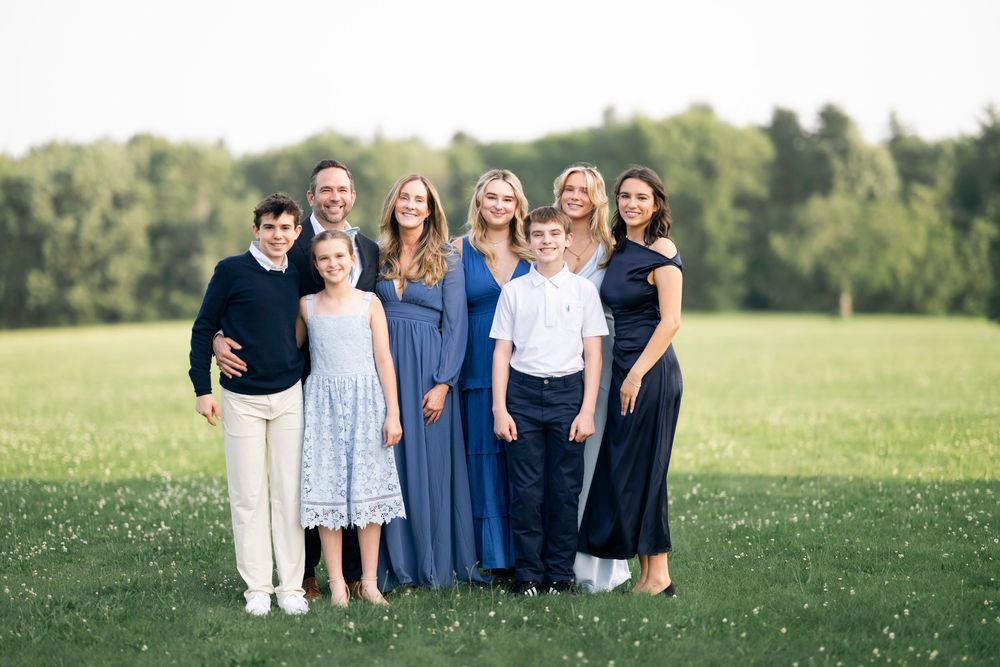 A group of people standing together on a grassy hill in formal attire for a special outdoor occasion.