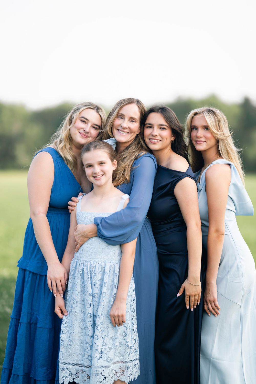 A group in coordinating blue and navy dresses pose together outdoors in a casual candid style.