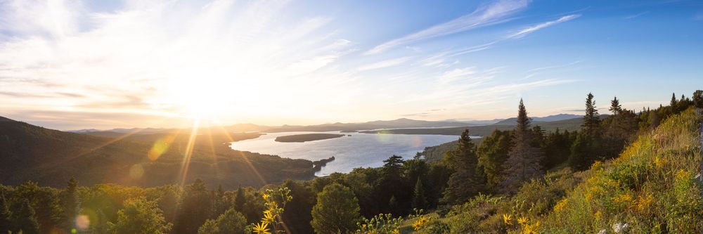 Stunning golden sunrise panorama over a scenic lake surrounded by lush green hills.