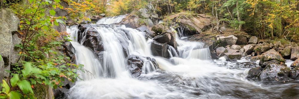 Panoramic view of a rushing waterfall cascading over rocks surrounded by autumn foliage.