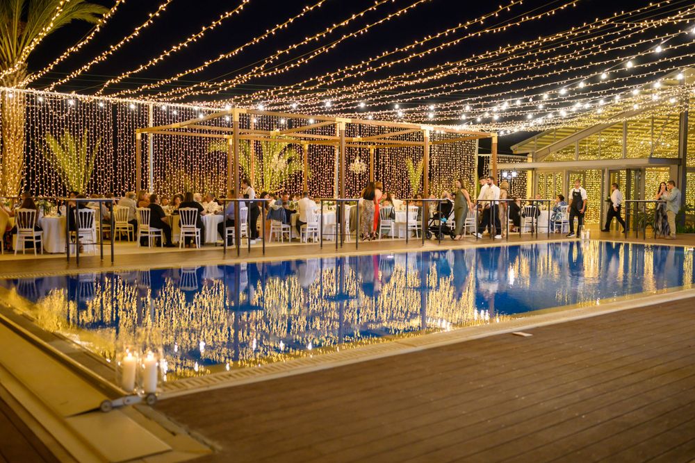 Elegant poolside venue decorated with string lights reflecting on calm water at night.