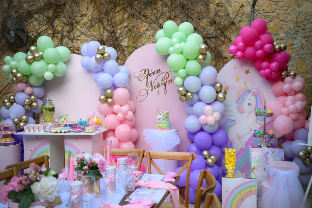 Colorful balloon arch installation with pastel pink, purple, and mint green balloons against a stone wall.