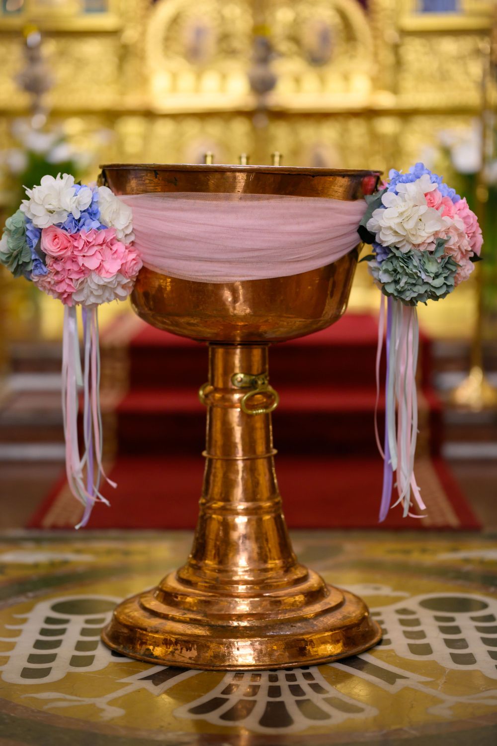 Ornate baptismal font decorated with pink and blue hydrangeas and white tulle ribbons.
