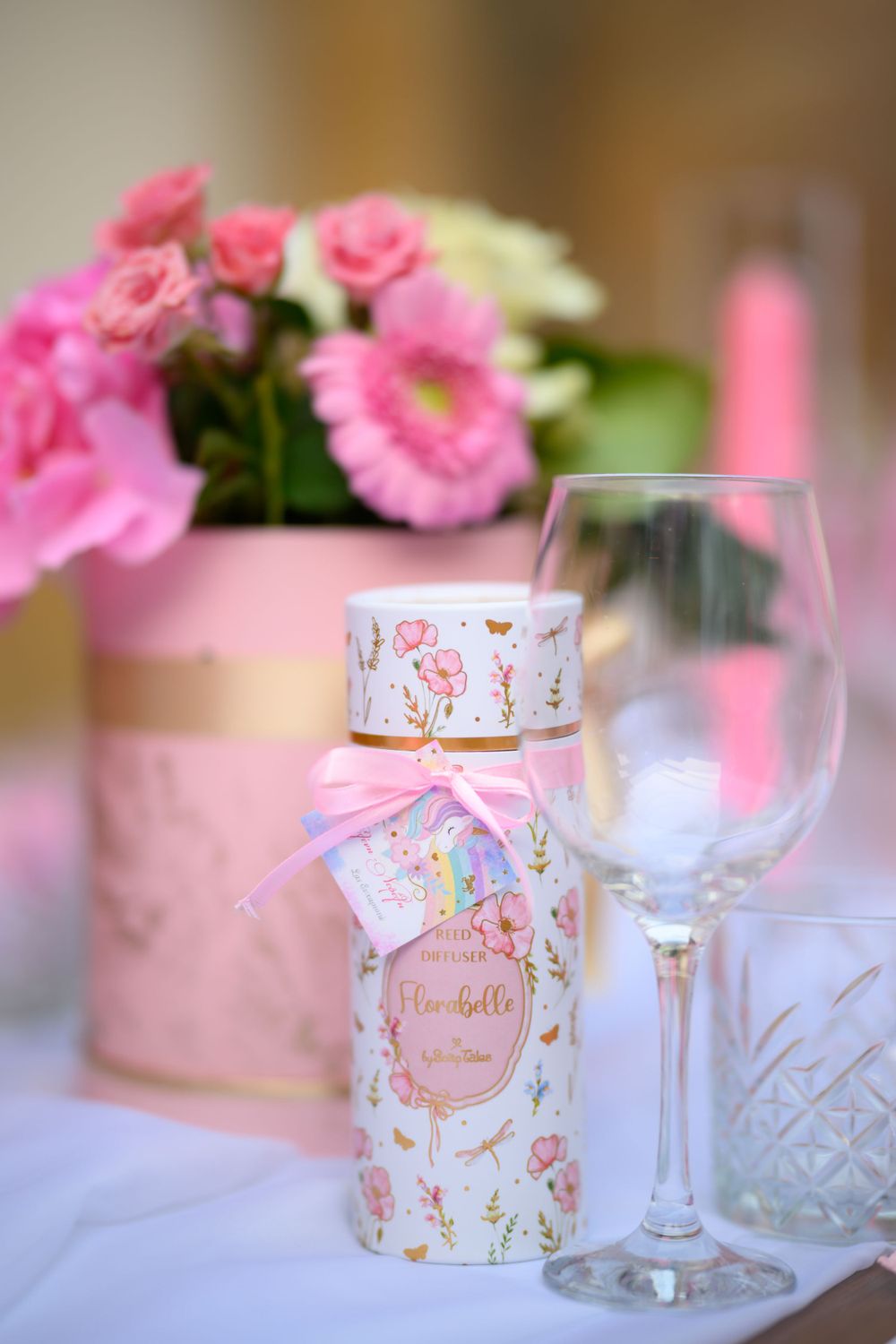 Pink floral centerpiece with decorative bottle and wine glass on white tablecloth.