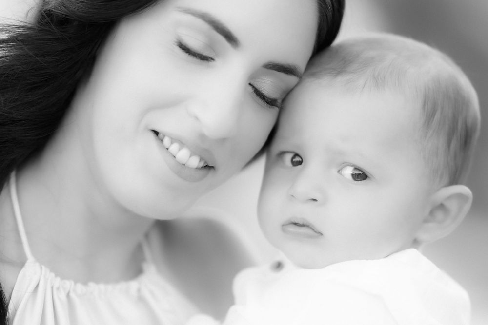 Intimate black and white portrait of parent and baby in soft lighting.
