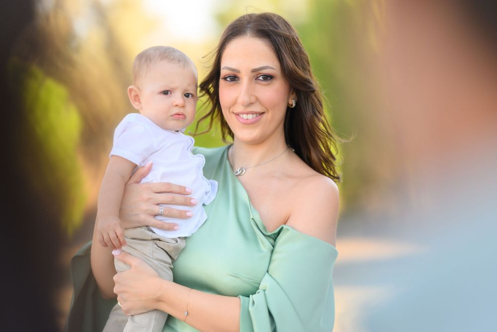 Parent holds baby while posing in sunlit outdoor setting.