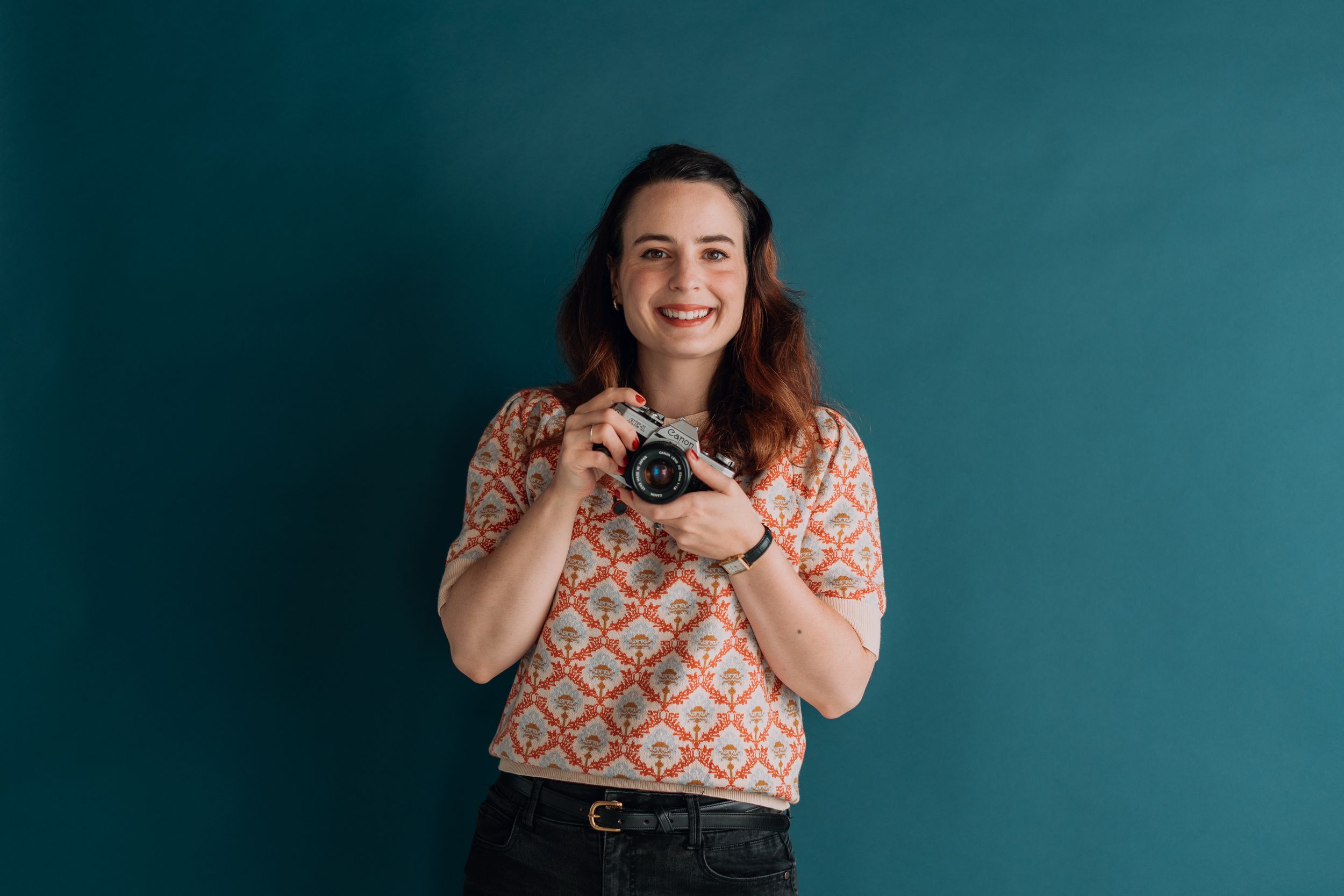 Person in floral print top posing against a teal blue studio backdrop.