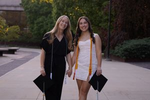 Woman holding hands with their graduation caps and regalia, smiling and excited to graduate for a graduation photoshoot