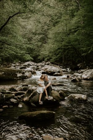 a couple sit on a big rock in the river in Western North Carolina just outside of Asheville