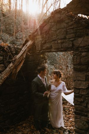 a bride and groom stand in the doorway of the ruins of an old river rock building in Western North Carolina near Asheville and Boone