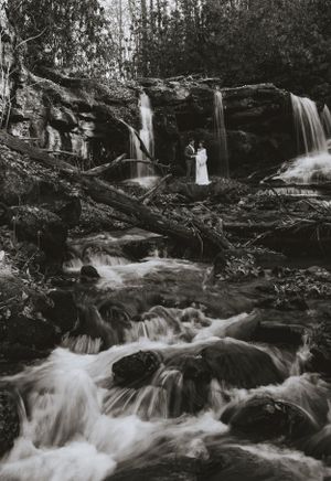 a black and white photo of a couple in the middle of a large waterfall scene that seems to be flowing slowly