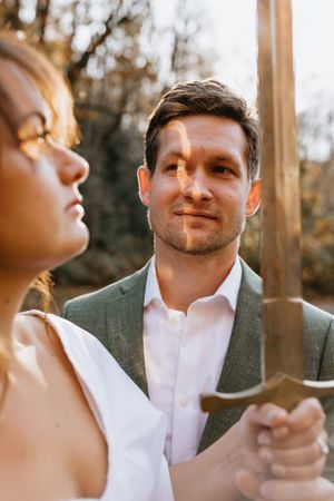 a couple holds a sword and the sun light cast a glare on the mans face in Western North Carolina near Asheville and Boone