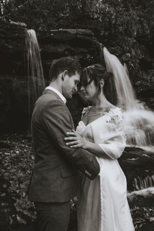 a black and white photo of a couple leaning their heads together in front of a waterfall