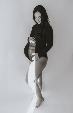 the light streams in on a mother to be standing in a white room