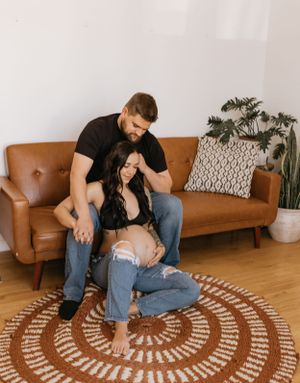 a mother and father to be sit on a leather couch with a circle striped rug
