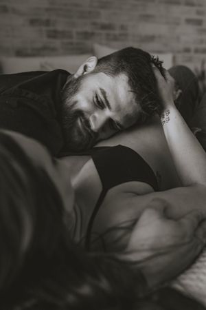 a father to be looks longingly at the mother of his child as he lays his head on her pregnant belly in black and white