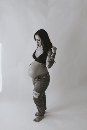 a monochrome shot of a mother to be standing in an all white room