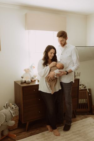a mom and dad in a beige nursery admire their infant son