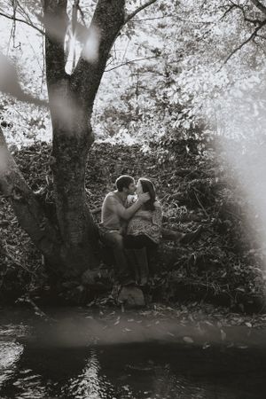 a couple in black and white are about to share a kiss beneath the tree on the bank of the river