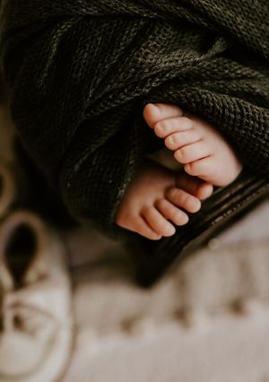 tiny baby toes poke out from under the green cloth he is wrapped in