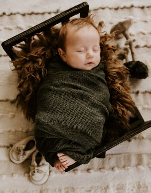 an infant baby is in a tiny bed wrapped in green cloth with his shoes beside him