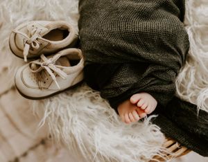 an infants toes poke out from under a green cloth with his shoes beside him