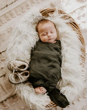 an infant baby wrapped in green cloth and placed in a basket with his shoes beside him