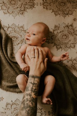 a tattooed mom lays her arm on her infant baby with a floral pattern in the background