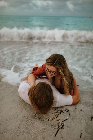 a couple laying on the beach in the breaking waves with blue water behind them in Anna Maria Island Florida