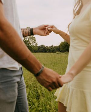 a man and woman hold hands with their arms making a circle framing the grassy field behind them