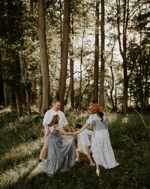 a family of 4 hold hands and play in a circle in the forest
