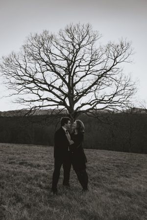 a monochrome shot of a couple kissing in front of a large tree with the Blueridge Mountains of Asheville in the background